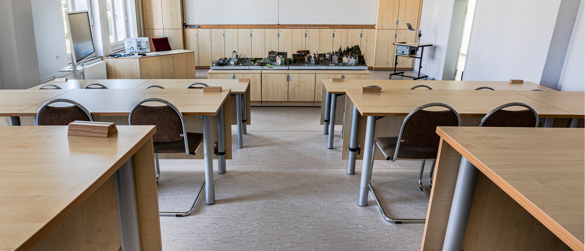 Ein leerer Hörsaal mit holzverkleideten Stühlen und Tischen.