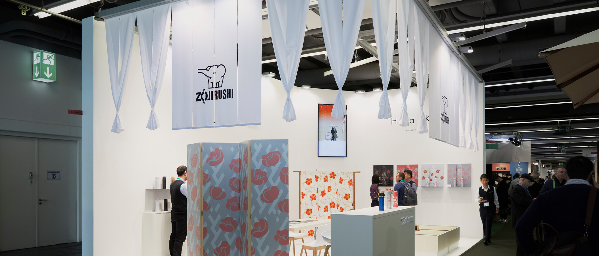 Vertreter:innen der Firma Zojirushi erklären diversen Kunden ihre Produktpalette auf einer Messe.